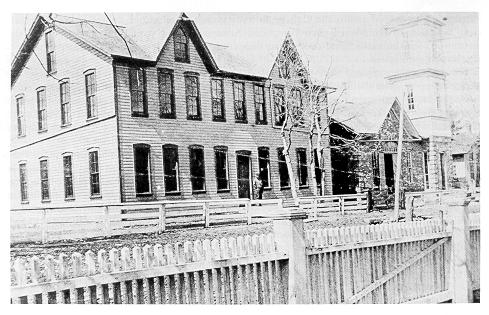 Old black and white photograph of the Mechanical Arts Building (left) and pump houses on unpaved street