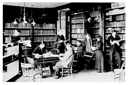 old black and white photograph of Fred Lewis Pattee and students in the library of Old Main. 