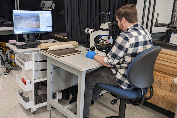 A student sitting at a desk using the the Olympus CX43 RF microscope to examine materials