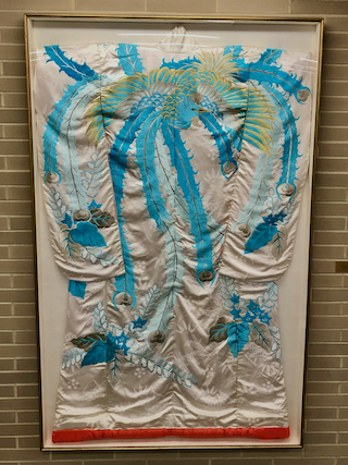 White silk kimono with intricate blue embroidery framed behind glass