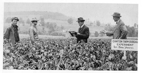 old black and white photograph of serveral men conversing in a farm field