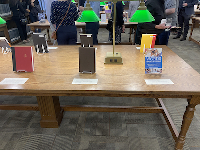 book selections from the 2022 promotion and tenure reception; books are displayed on a wood table lit by lamps with green glass shades